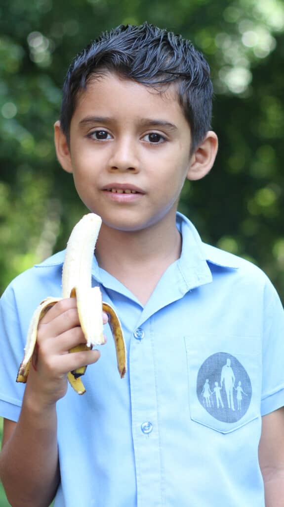 Ein Junge in einem NPH-Hemd hält eine Banane in der Hand.