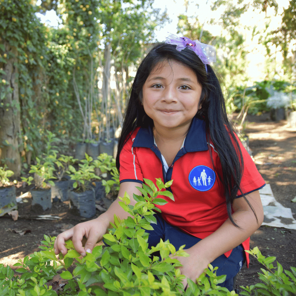 Ein Mädchen vom NPH Guatemala hockt vor ihrem grünen Kräutern.